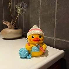 Personnage canard jaune avec un bonnet et une pelote bleue